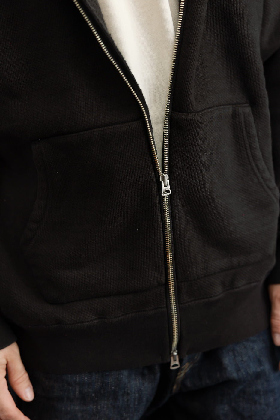 Close-up of the front zipper and pocket of a black zip-up hoodie on a male model.