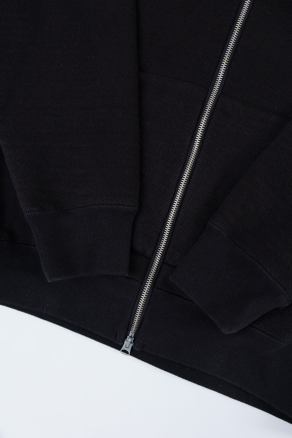 Close-up of the front center zipper and ribbed hem of a black zip-up hoodie.