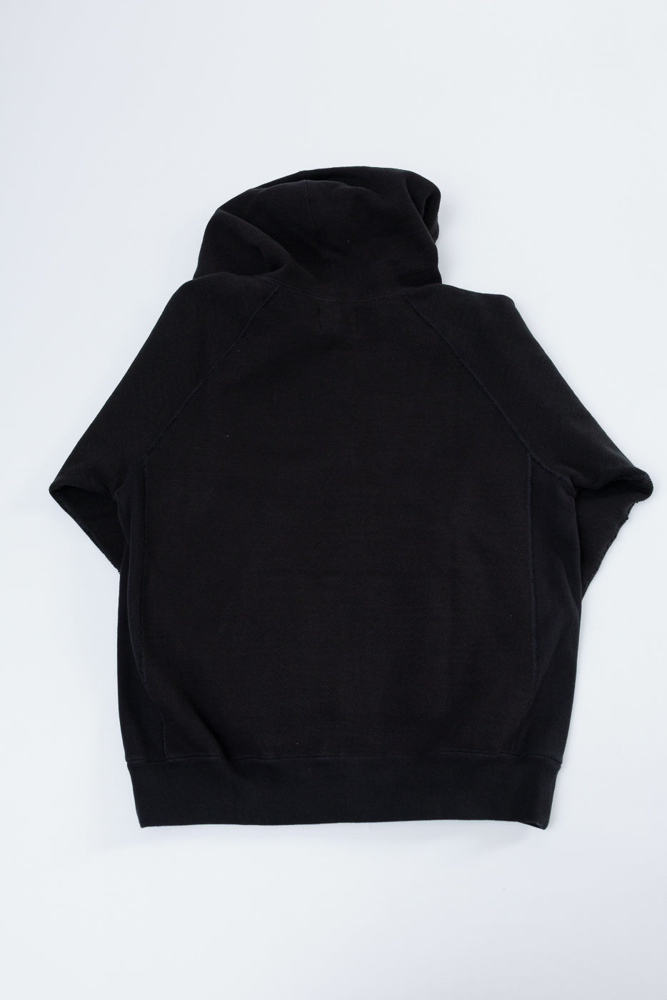 Flat lay showing the back of a black hooded sweatshirt with a ribbed hem.