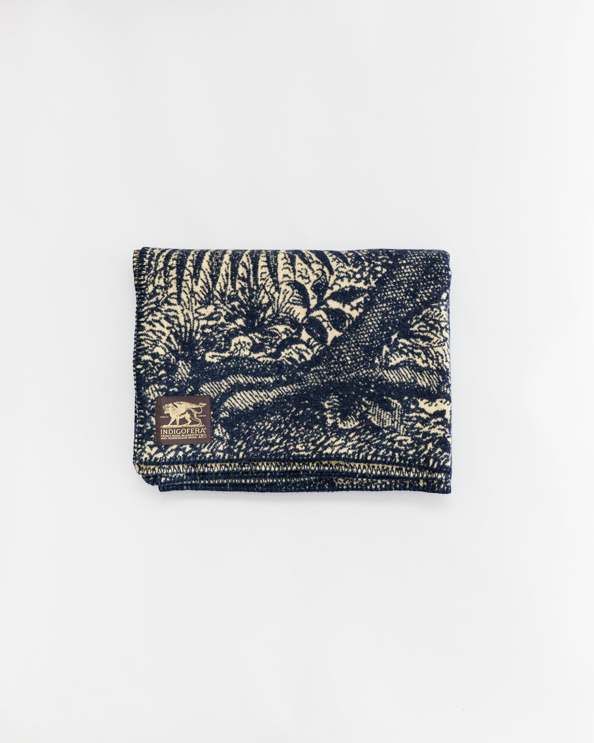 Flat lay of folded beige and navy blanket, front side, with woven graphic and logo tag detail
