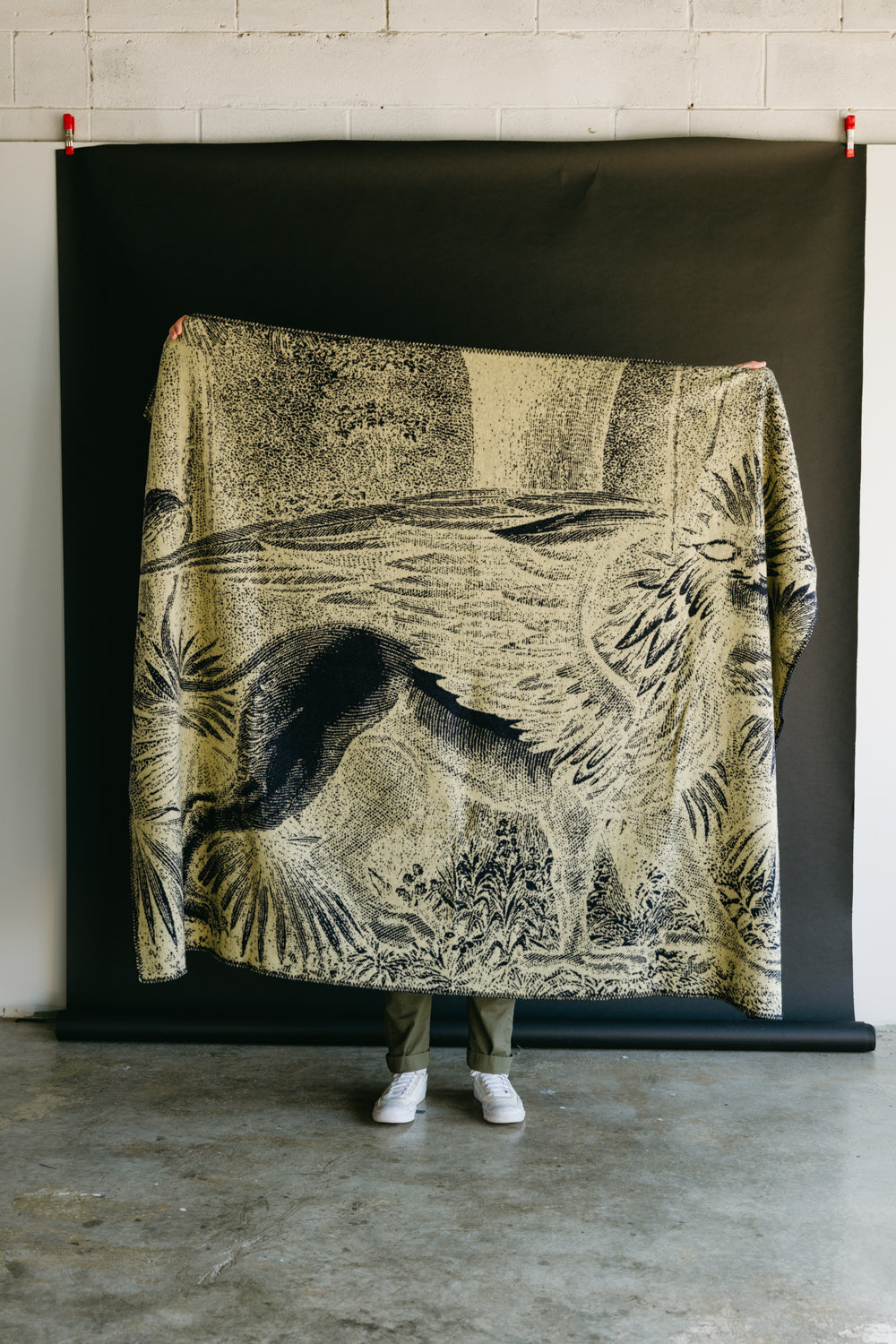 Full body, front view of beige and navy patterned blanket held by male model, only legs visible.