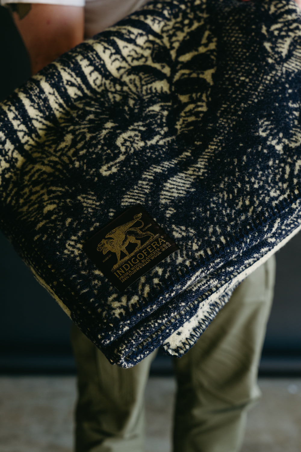 Close-up of male model holding folded beige navy wool blanket, showing front side and brand tag.