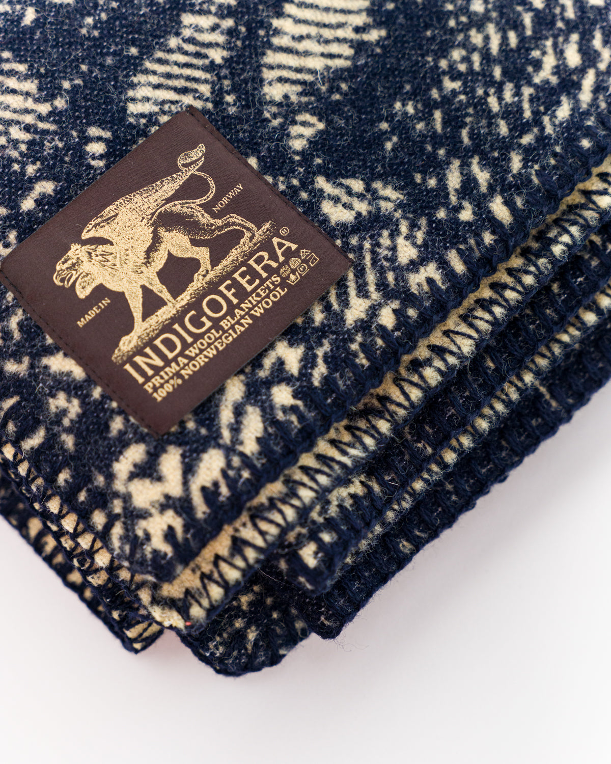 Close-up of folded beige and navy wool blanket, showing corner, fabric texture, and woven label.