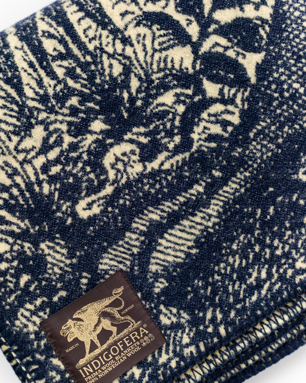 Close-up of beige and navy wool blanket front, showing textured fabric and branded tag detail.