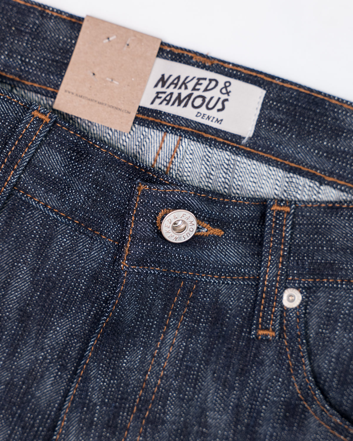 Close-up front view of Naked & Famous Big Slub Selvedge denim jeans, showing waistband, top button, fabric texture, and branded label detail.