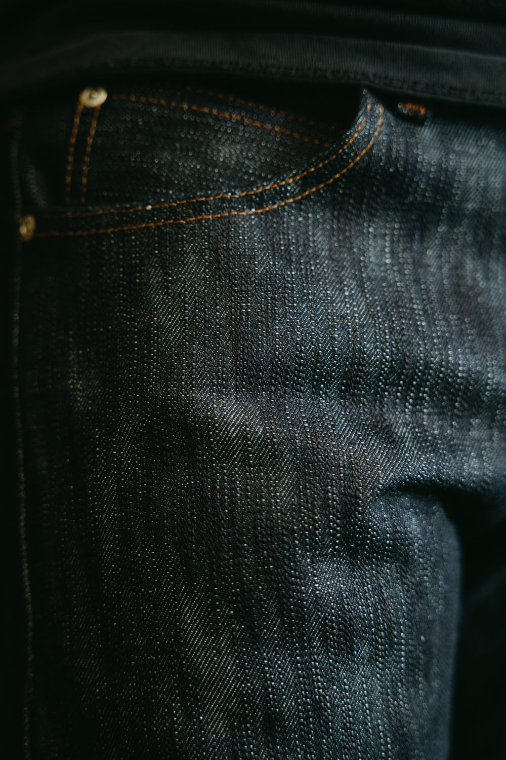 Close-up of Naked & Famous Big Slub Selvedge jeans front pocket, textured raw denim, orange stitching.