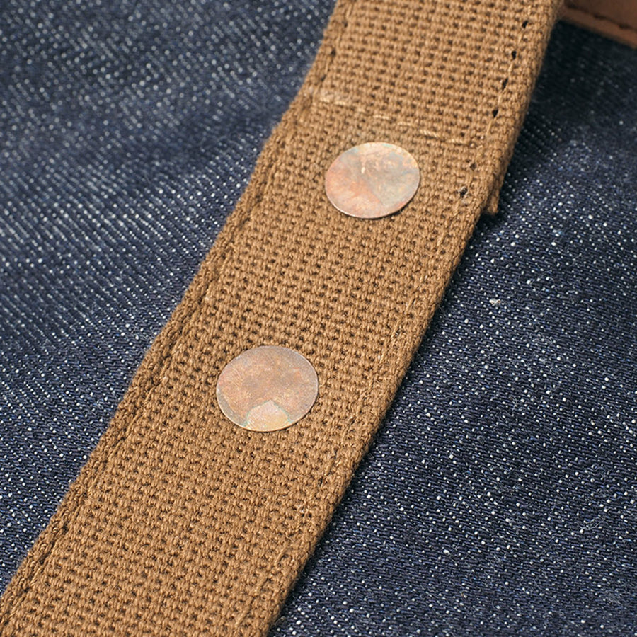 Close-up of denim tote bag front, showing brown textured handle with metal rivets.