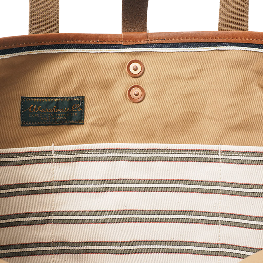 Close-up of tote bag interior showing striped fabric lining, leather trim, snap buttons, and interior label.