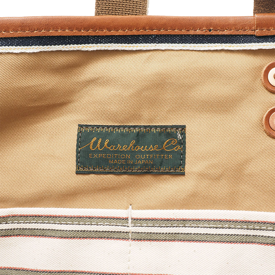 Close-up of inside top edge of denim tote bag showing label, stitching, and rivet details.